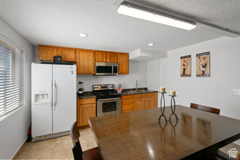 Kitchen with stainless steel appliances, dark countertops, brown cabinetry, recessed lighting, and light tile patterned floors