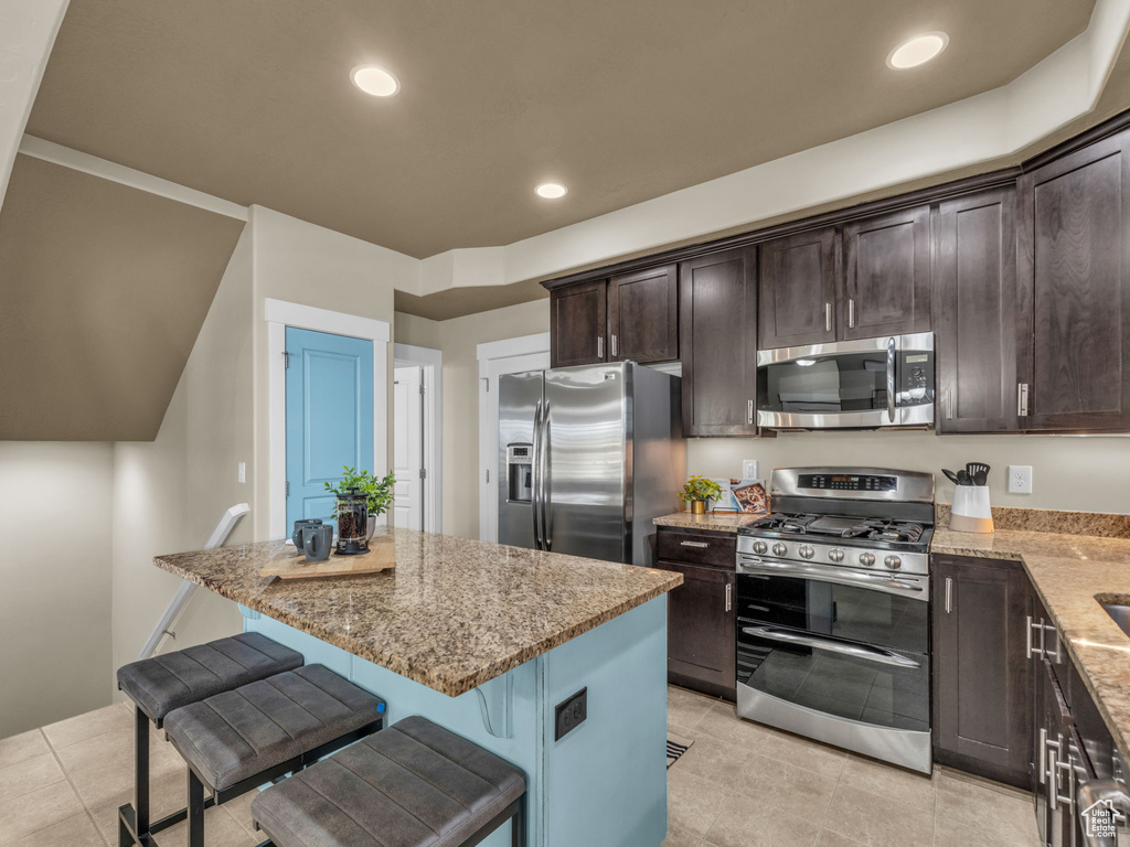 Kitchen with appliances with stainless steel finishes, light stone counters, dark brown cabinetry, a kitchen island, and recessed lighting
