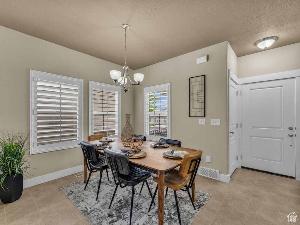 Dining area featuring a chandelier, light tile patterned floors, and a textured ceiling