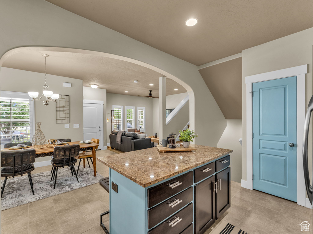 Kitchen with arched walkways, a chandelier, light stone countertops, pendant lighting, and recessed lighting