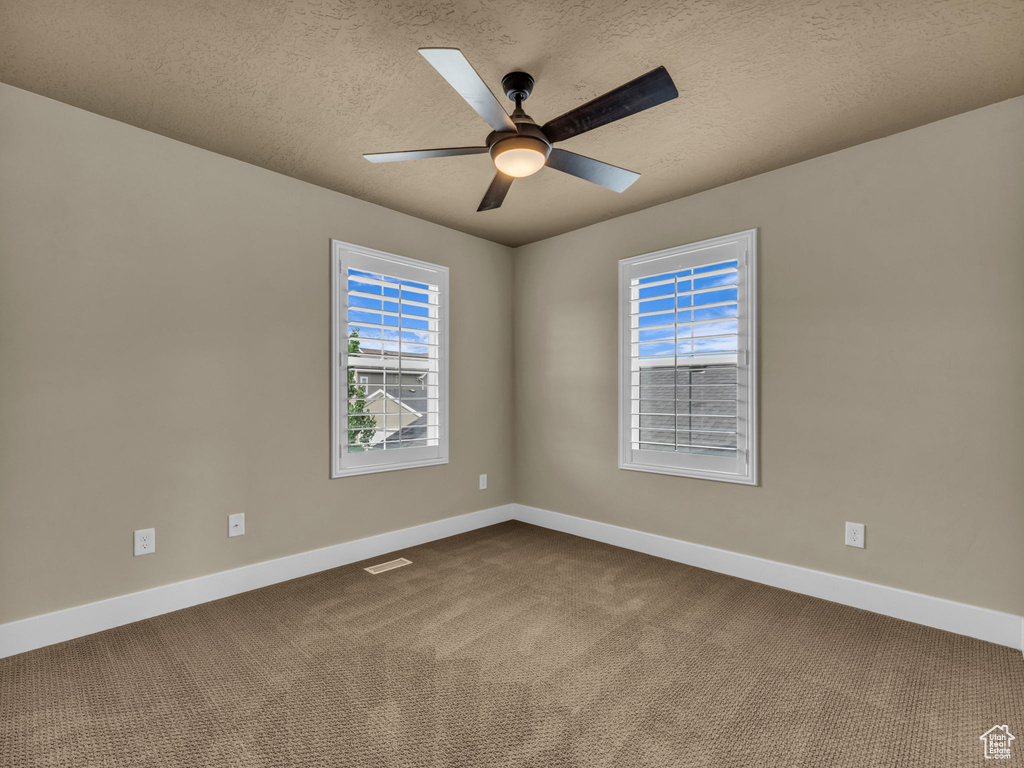 Empty room with dark carpet, a ceiling fan, and a textured ceiling