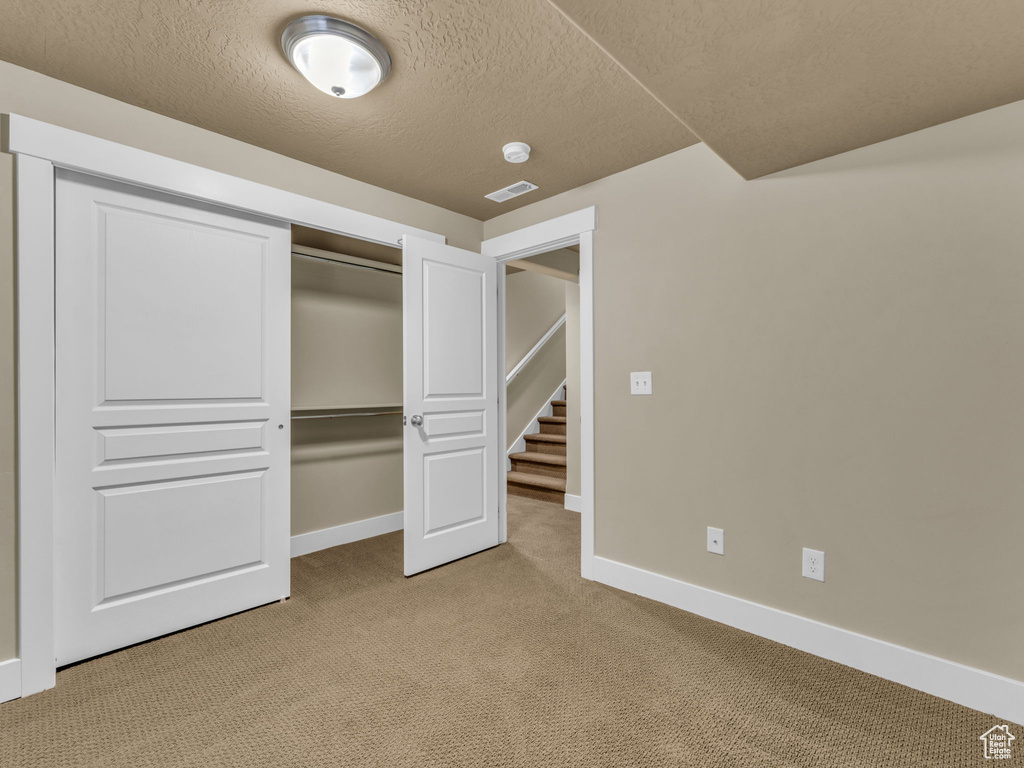 Unfurnished bedroom featuring light carpet, a textured ceiling, and a closet