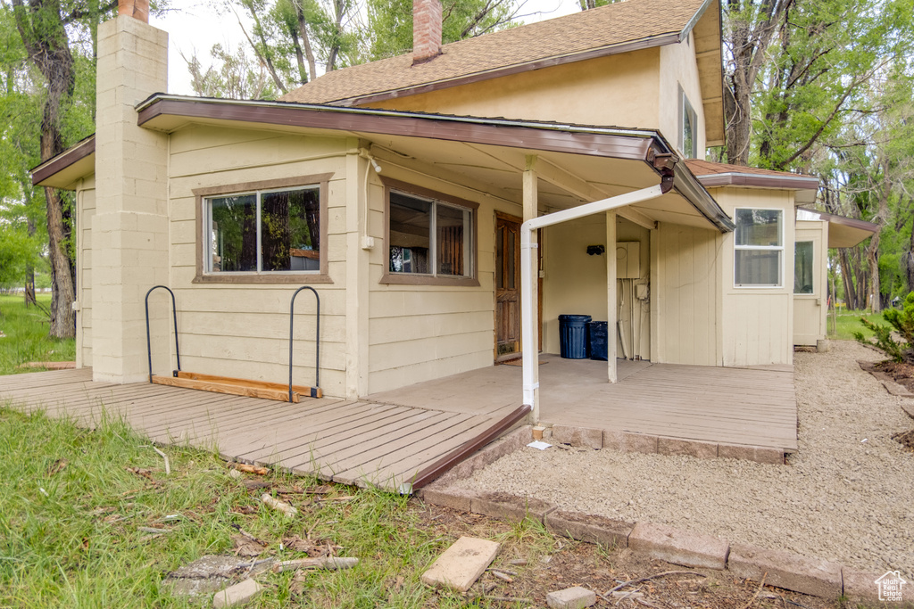 Back of house featuring a chimney, a shingled roof, and a wooden deck