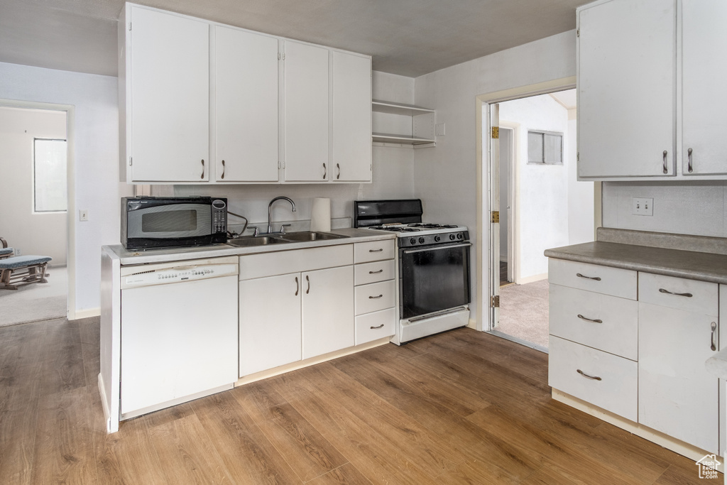 Kitchen featuring white dishwasher, gas range, black microwave, wood finished floors, and white cabinets