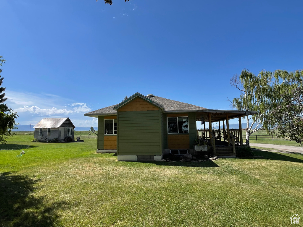 Rear view of property with a yard, covered porch, and roof with shingles