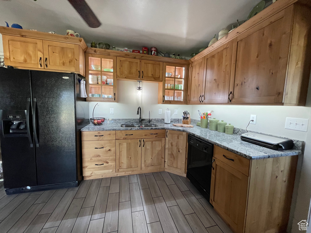 Kitchen with black appliances, wood finish floors, light stone countertops, and glass insert cabinets