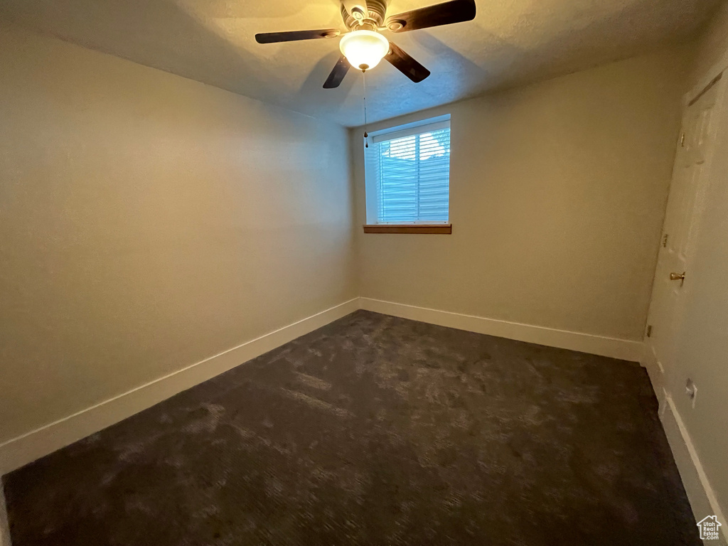 Unfurnished room with dark carpet and ceiling fan