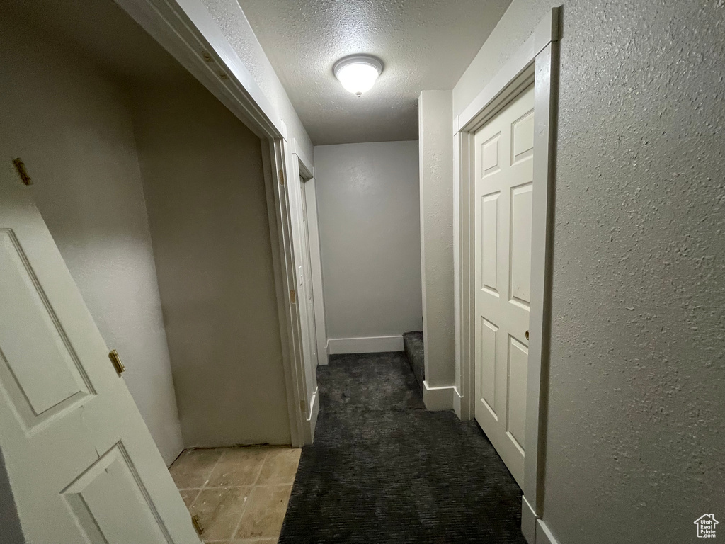Corridor featuring a textured ceiling, carpet, and a textured wall