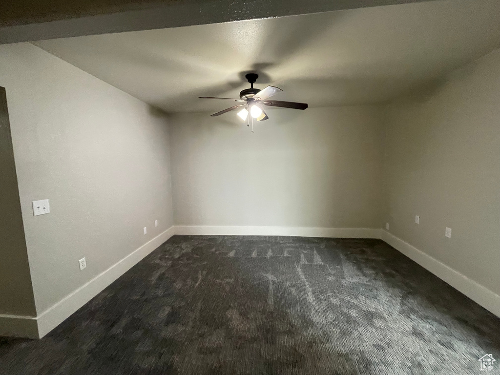 Empty room featuring dark colored carpet and a ceiling fan