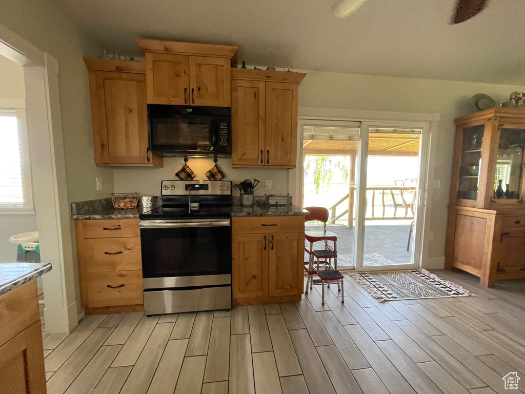 Kitchen with black microwave, stainless steel electric stove, wood tiled floors, and dark stone countertops