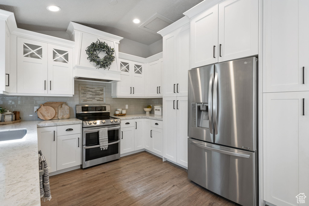 Kitchen featuring appliances with stainless steel finishes, white cabinetry, tasteful backsplash, wood finished floors, and recessed lighting