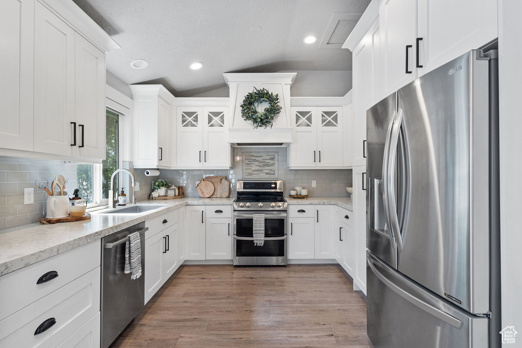 Kitchen with appliances with stainless steel finishes, vaulted ceiling, white cabinetry, and recessed lighting