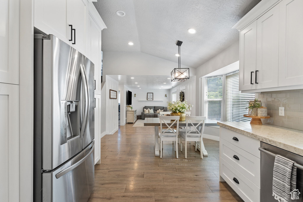Kitchen with appliances with stainless steel finishes, vaulted ceiling, open floor plan, backsplash, and white cabinetry