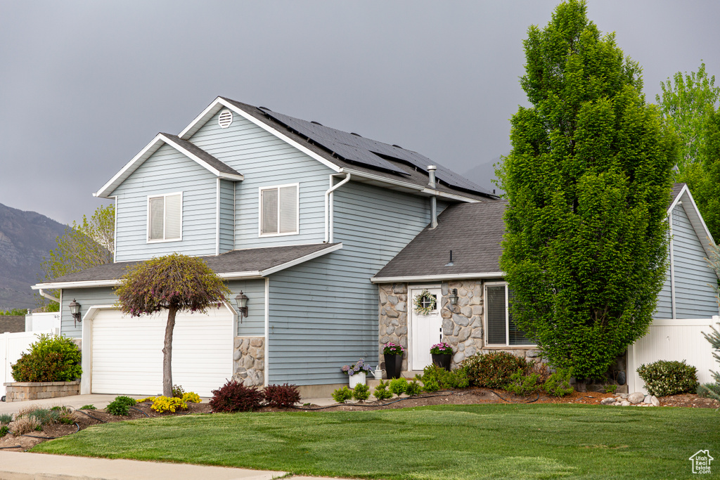 Traditional-style house featuring stone siding, roof mounted solar panels, an attached garage, a mountain view, and driveway