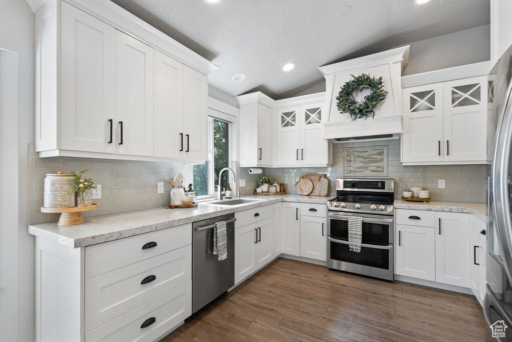 Kitchen featuring stainless steel appliances, lofted ceiling, white cabinetry, backsplash, and glass insert cabinets