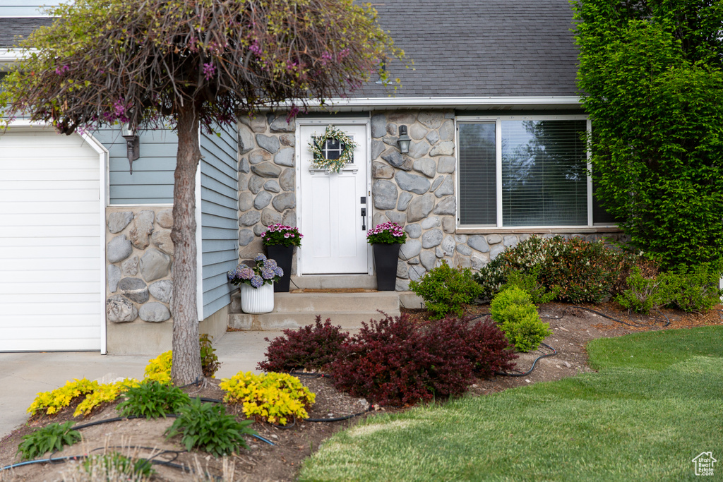 Doorway to property featuring stone siding and a shingled roof
