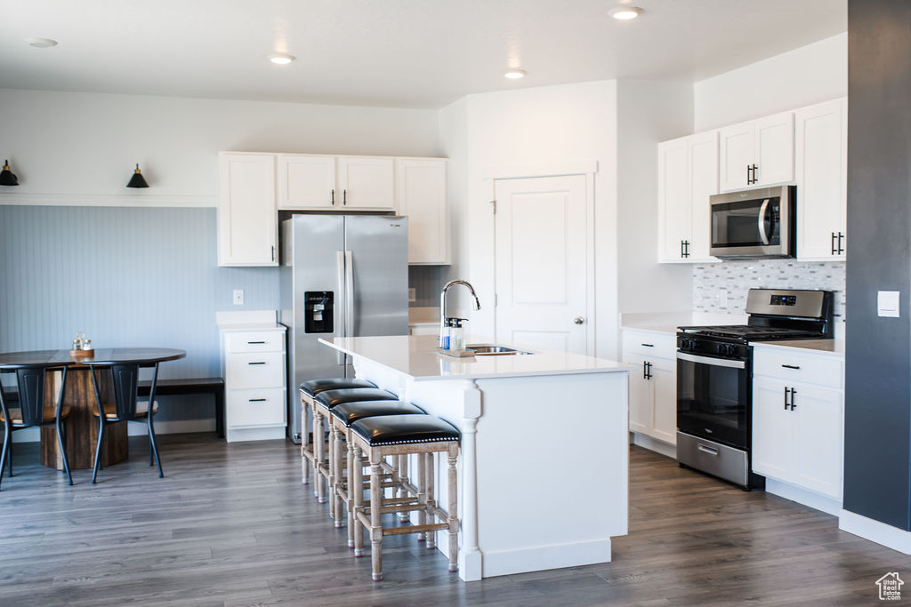 Kitchen with stainless steel appliances, a kitchen breakfast bar, a center island with sink, decorative backsplash, and light countertops