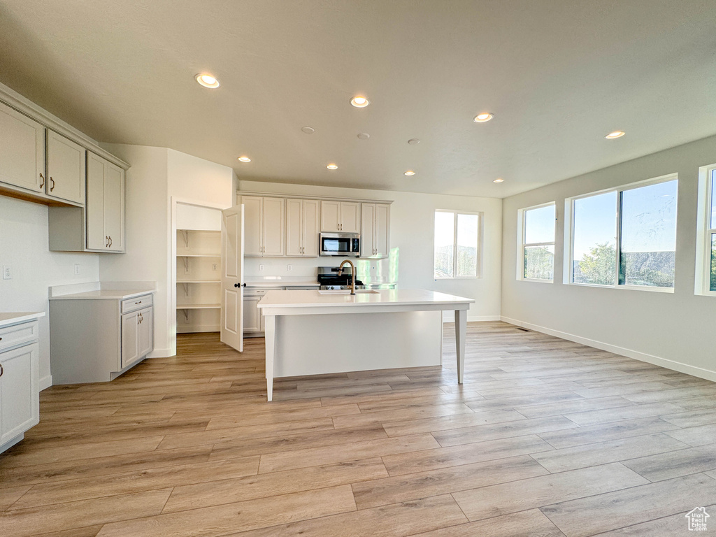 Kitchen with stainless steel microwave, recessed lighting, light wood-style floors, a kitchen island with sink, and light countertops
