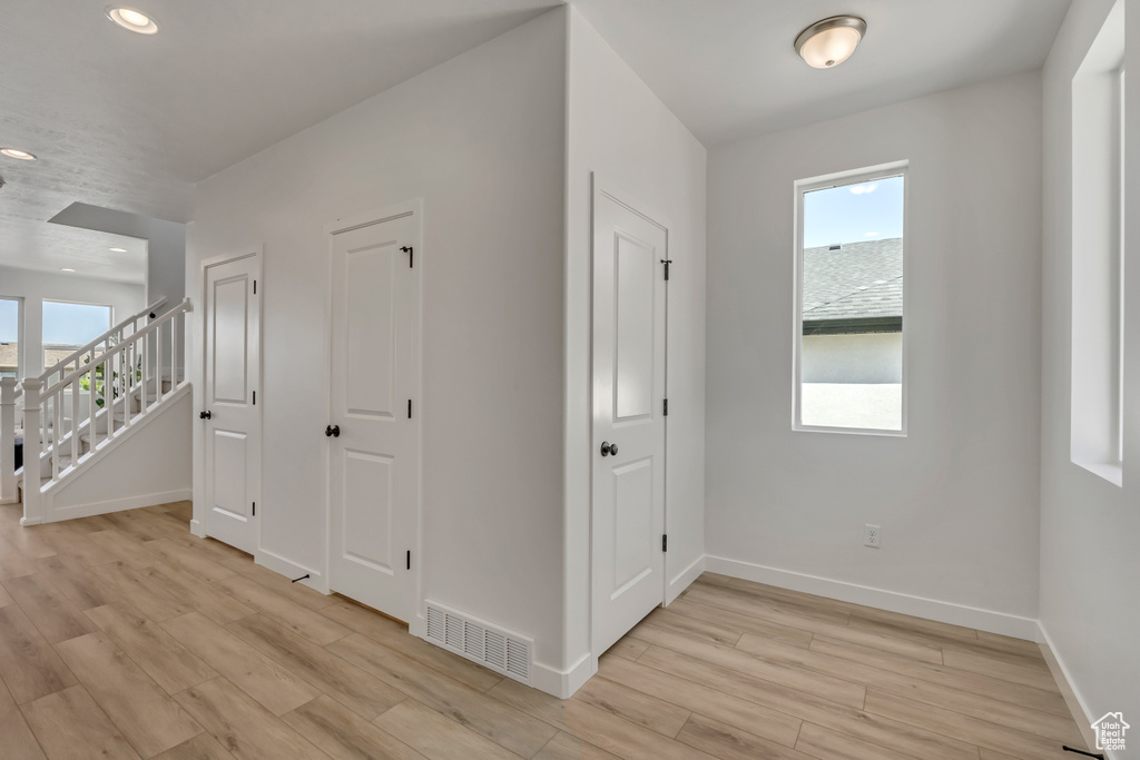 Hall with plenty of natural light, light wood-style flooring, recessed lighting, and stairs