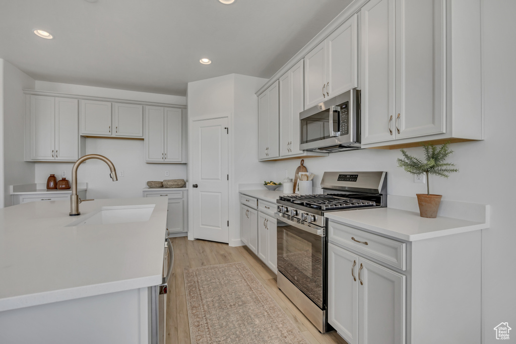 Kitchen with stainless steel appliances, recessed lighting, light wood finished floors, light countertops, and white cabinets