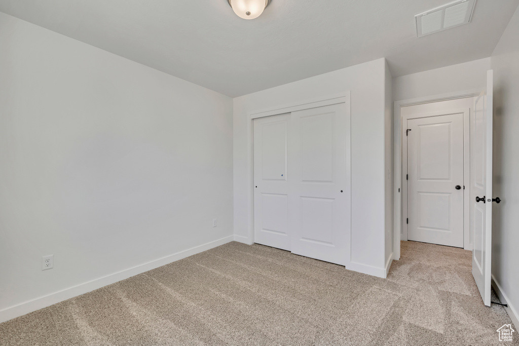 Unfurnished bedroom with light colored carpet and a closet