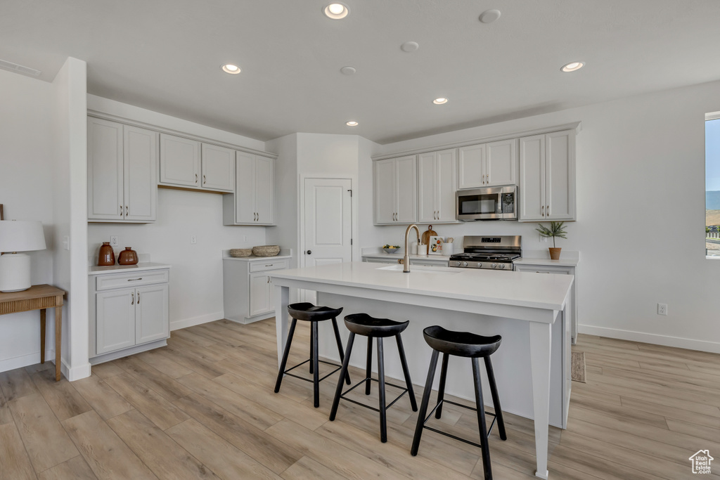 Kitchen with stainless steel appliances, light wood finished floors, recessed lighting, a kitchen bar, and light countertops