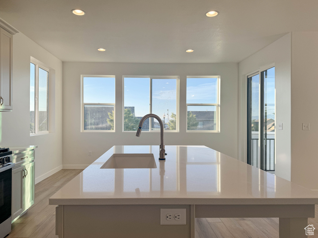 Kitchen featuring an island with sink, recessed lighting, light wood-style floors, stainless steel range, and light stone countertops