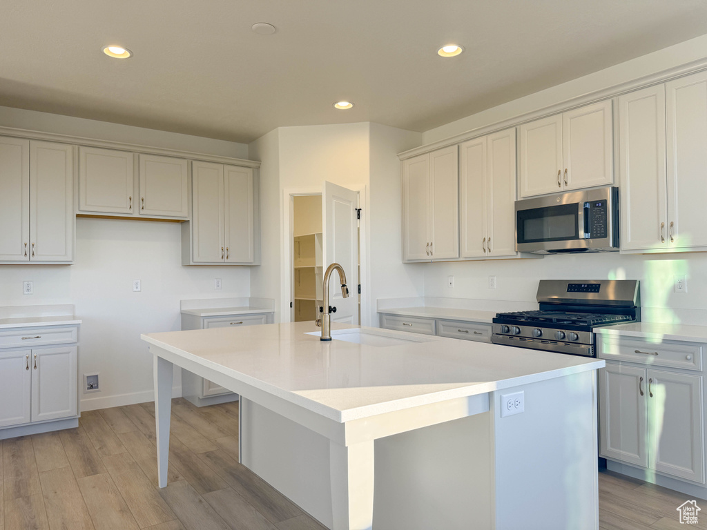 Kitchen featuring appliances with stainless steel finishes, a kitchen island with sink, light wood finished floors, recessed lighting, and light countertops