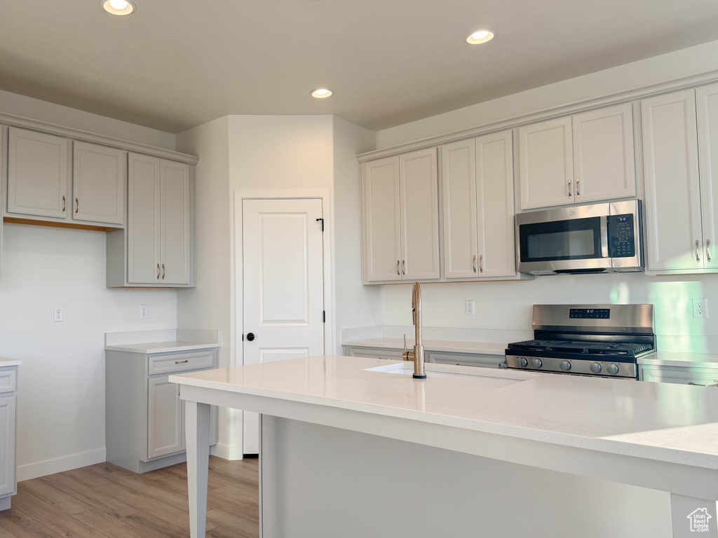Kitchen featuring appliances with stainless steel finishes, light wood finished floors, recessed lighting, light countertops, and a kitchen bar