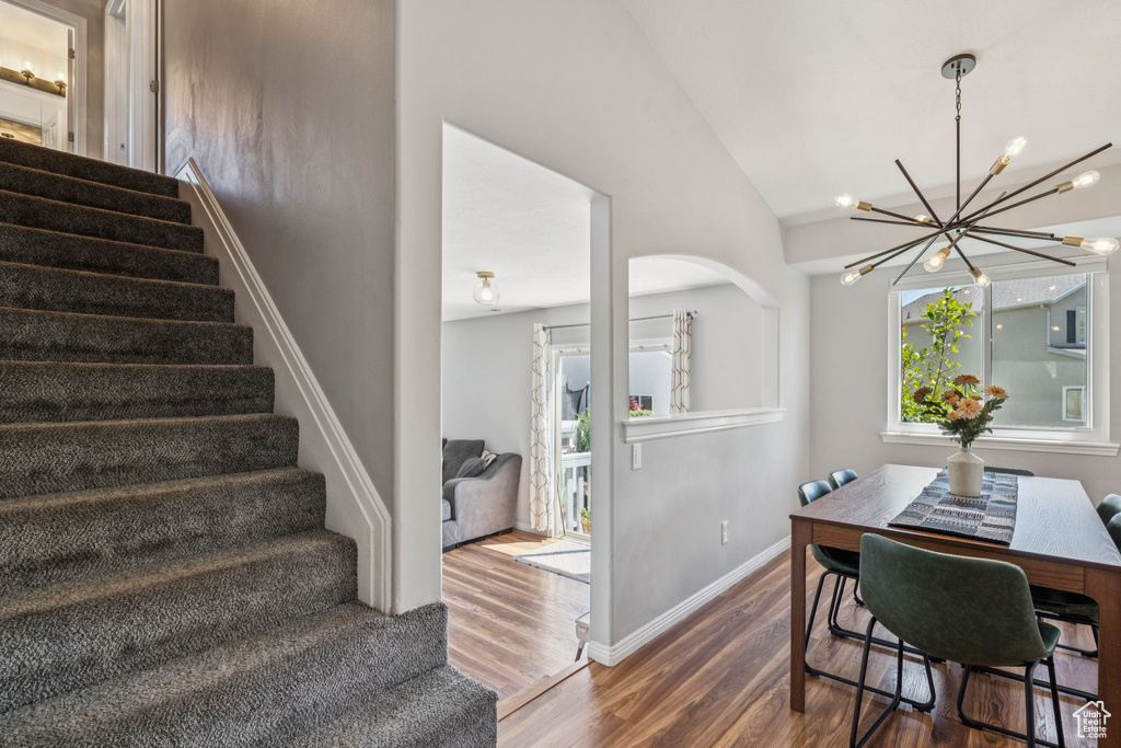 Dining room featuring stairs, wood finished floors, a chandelier, and high vaulted ceiling