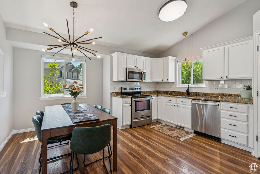 Kitchen featuring stainless steel appliances, decorative backsplash, a chandelier, white cabinetry, and vaulted ceiling