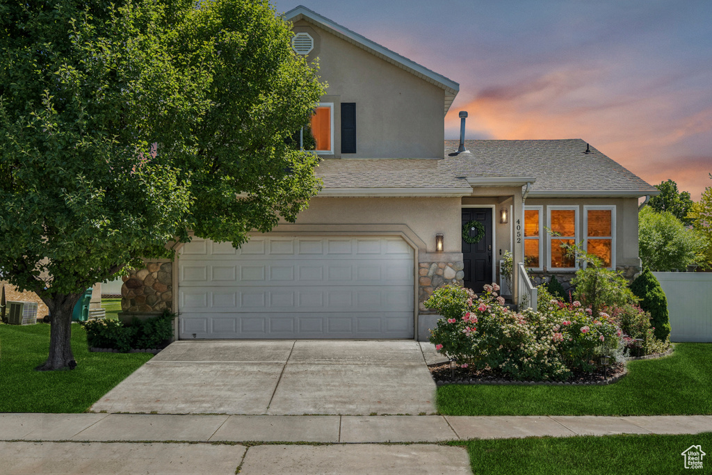 View of front facade featuring stucco siding, stone siding, driveway, an attached garage, and a front yard
