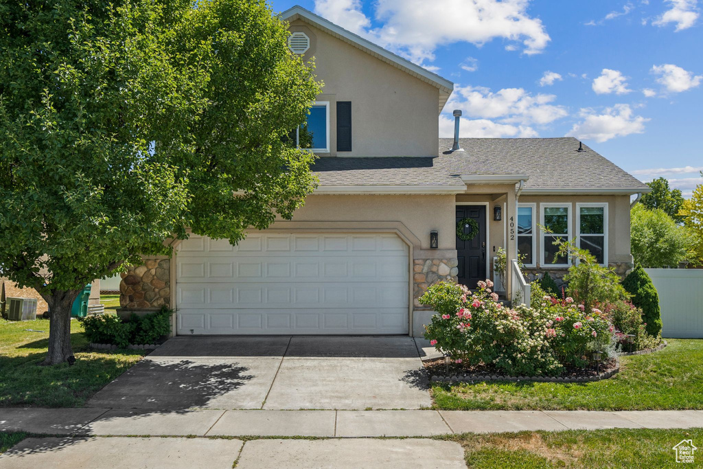 View of front facade featuring stone siding, stucco siding, driveway, and a garage