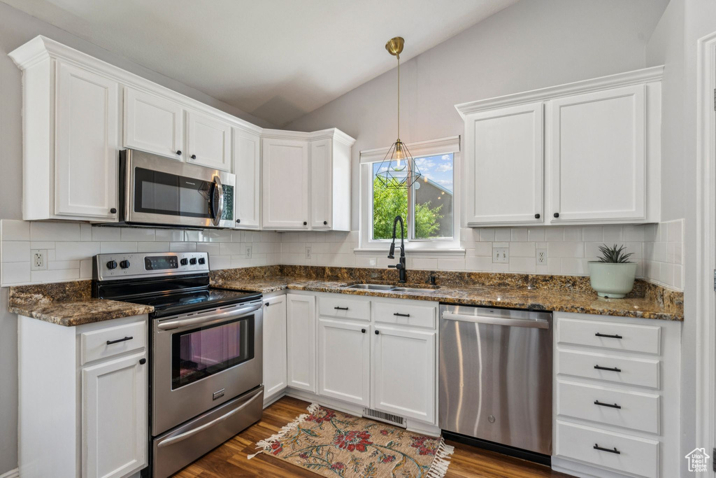 Kitchen with stainless steel appliances, white cabinets, lofted ceiling, tasteful backsplash, and dark wood finished floors