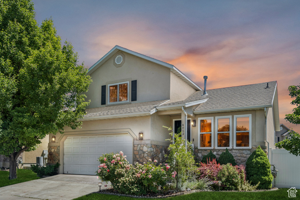 View of front facade with stone siding, stucco siding, roof with shingles, an attached garage, and driveway