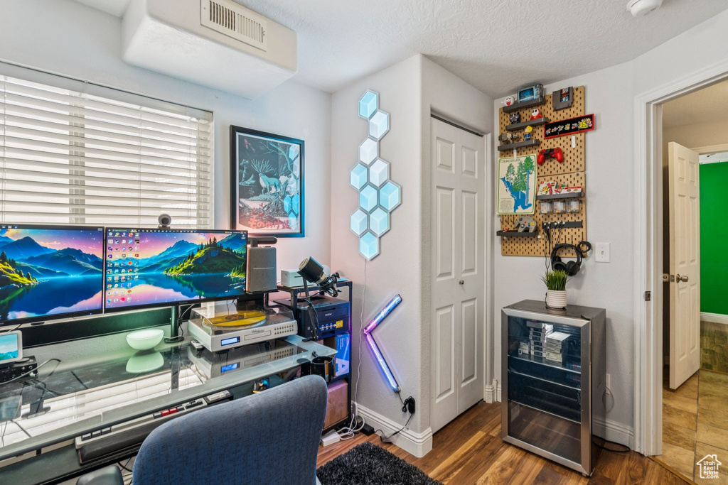 Office area with wine cooler, wood finished floors, and a textured ceiling