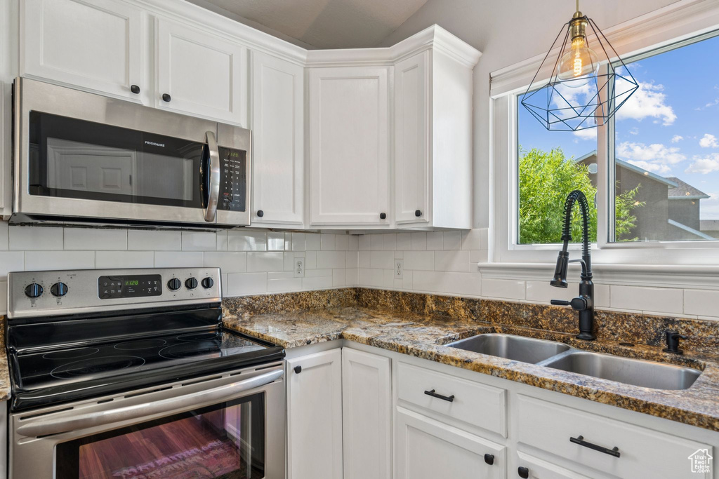 Kitchen with stainless steel appliances, white cabinets, decorative backsplash, dark stone countertops, and pendant lighting