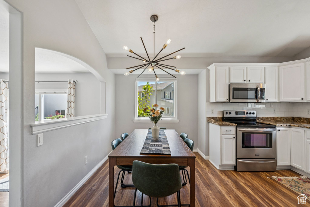 Kitchen featuring stainless steel appliances, a chandelier, white cabinetry, tasteful backsplash, and vaulted ceiling