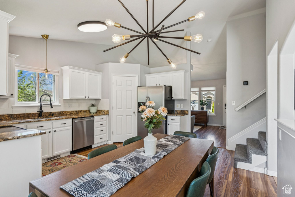 Kitchen featuring stainless steel appliances, white cabinets, decorative light fixtures, tasteful backsplash, and dark wood-type flooring