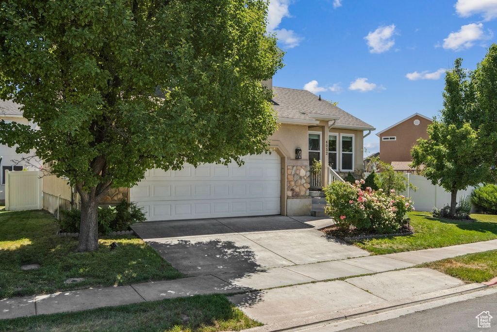 Obstructed view of property featuring stone siding, driveway, an attached garage, stucco siding, and roof with shingles