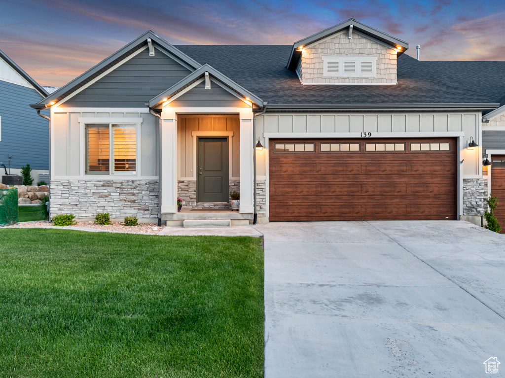 View of front facade featuring board and batten siding, an attached garage, a shingled roof, concrete driveway, and a front yard