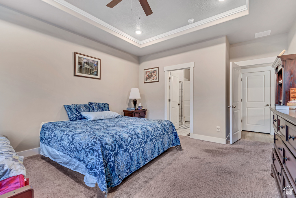 Bedroom featuring a raised ceiling, baseboards, crown molding, light colored carpet, and a ceiling fan