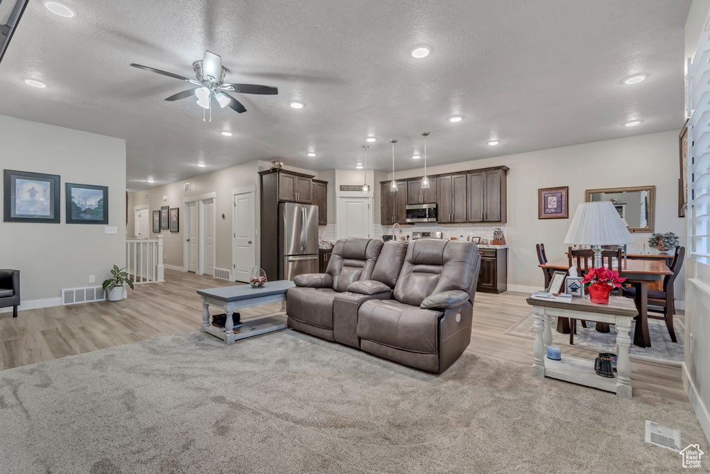 Living room with ceiling fan, light wood-style flooring, baseboards, recessed lighting, and a textured ceiling