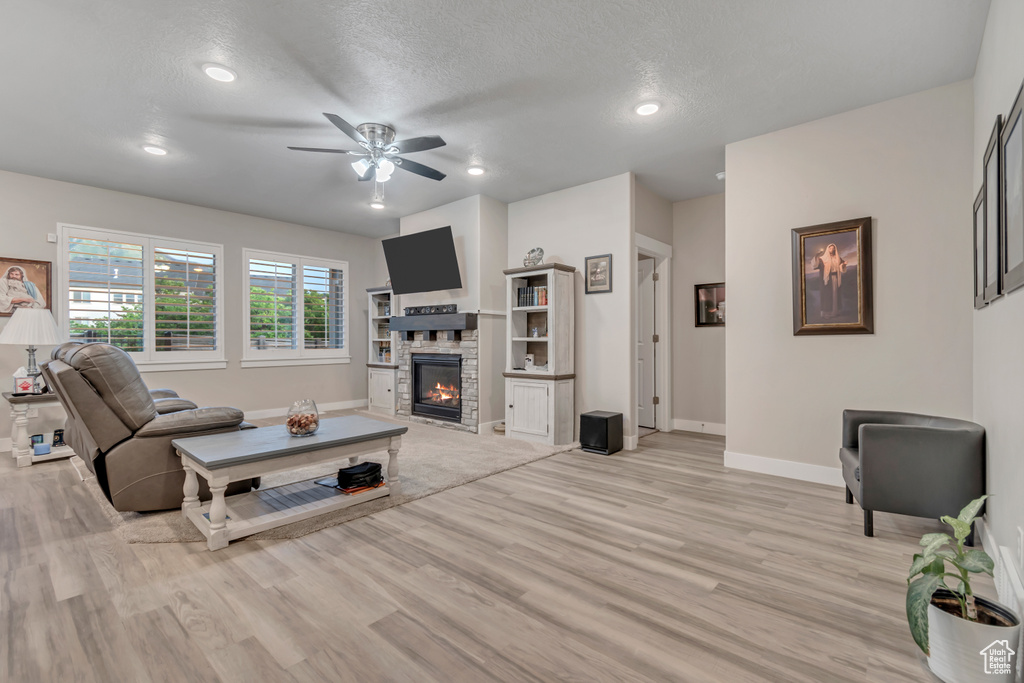 Living room featuring light wood-type flooring, baseboards, ceiling fan, a stone fireplace, and recessed lighting