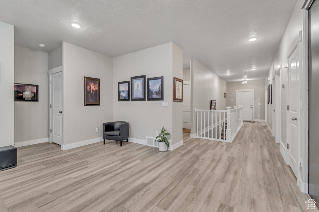 Hall with an upstairs landing, light wood-type flooring, baseboards, and a textured ceiling