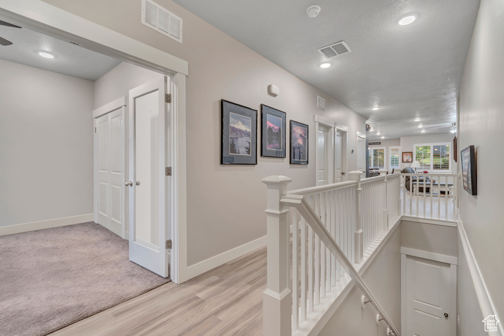 Hall with an upstairs landing, light wood finished floors, baseboards, and recessed lighting