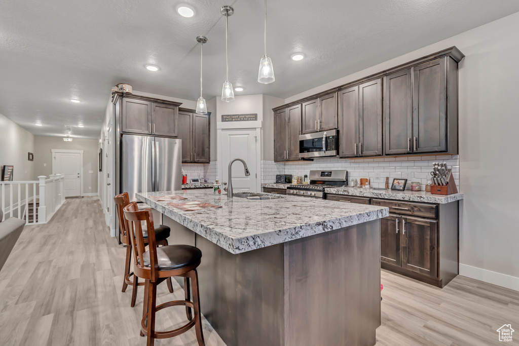 Kitchen featuring stainless steel appliances, baseboards, dark brown cabinetry, a sink, and backsplash