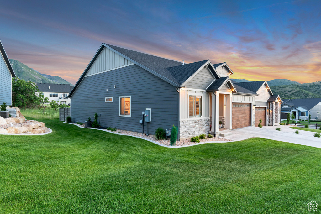 Property exterior at dusk with board and batten siding, concrete driveway, a mountain view, a garage, and a yard