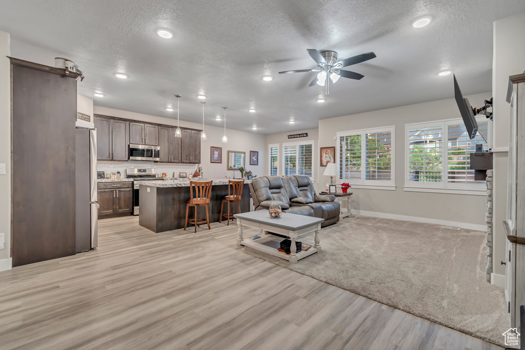 Living room featuring baseboards, light wood-type flooring, a textured ceiling, a ceiling fan, and recessed lighting