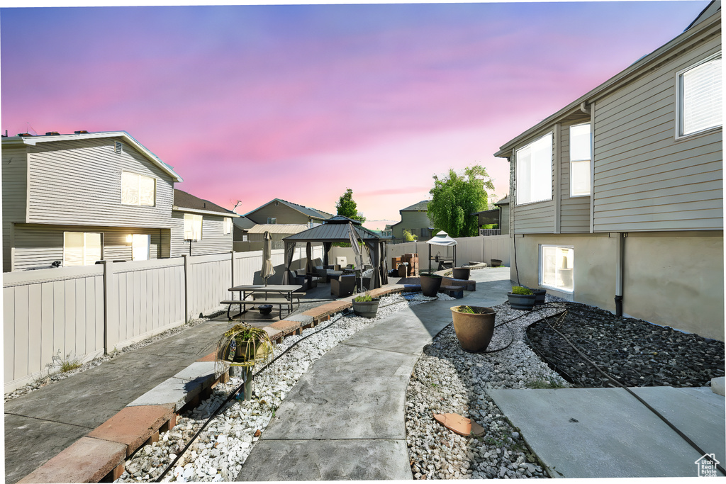 Patio terrace at dusk with a gazebo, a patio area, a fenced backyard, a residential view, and an outdoor hangout area